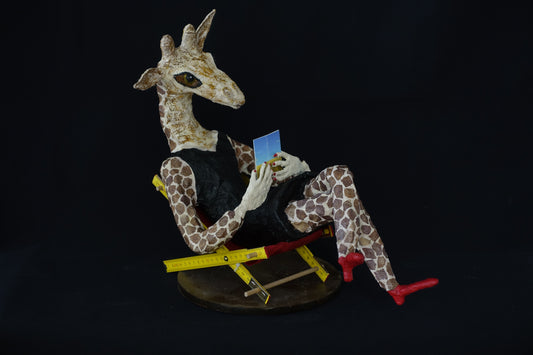 "lesende weibliche Giraffe im Kleinen Schwarzen mit roten Fingernägeln", figurative Skulptur / Mensch-Tier-Hybridwesen aus Drahtgeflecht, Gipsbinden, bedrucktem Papier und Acryl, schwarz und rote Schuhe, auf Liegestuhl sitzend