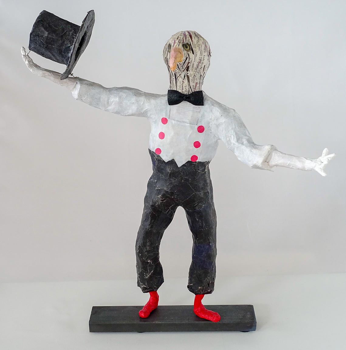 "Pantomime mit Greifvogelkopf und schwenkendem Zylinder", frei nach Marcel Marceau, figurative Skulptur / Mensch-Tier-Hybridwesen aus Drahtgeflecht, Gipsbinden, bedrucktem Papier und Acryl, und rote Schuhe auf Eisenplatte