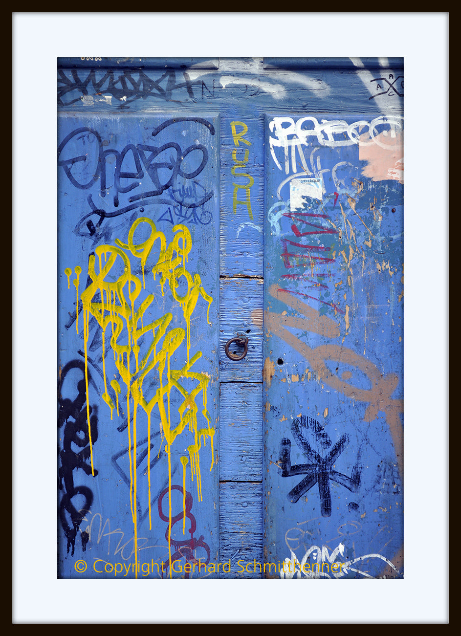 Graffito, mit gelben, weißen und roten Fantasiezeichen beschriftete Holztür, dominanter Komplementärkontrast blau-gelb
